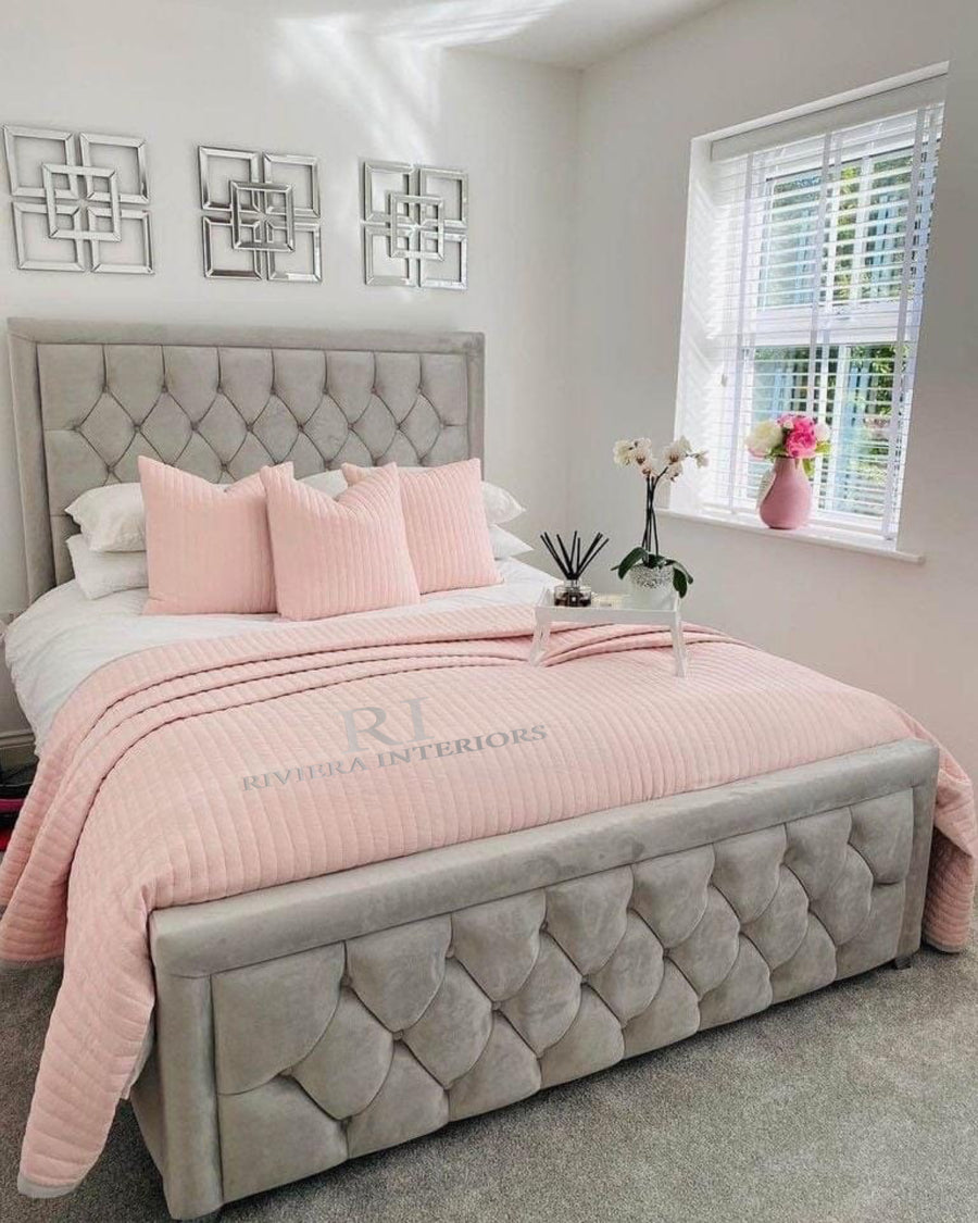 A modern bedroom with a tufted grey upholstered bed frame, with pink and white bedding and modern wall frames. 